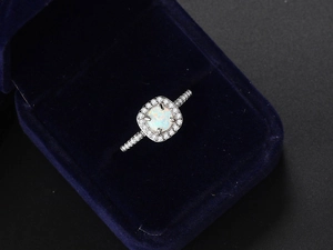 Close-up of a white opal engagement ring with pavé diamonds in a blue velvet box