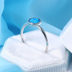 Minimalist silver ring featuring a round blue opal gemstone in a white velvet box