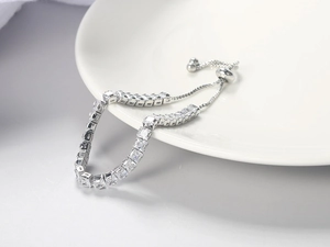 Detail of silver tennis bracelet with square zircons on white ceramic plate edges