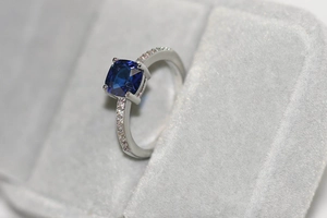 Gros plan d'une bague saphir bleu taille coussin avec pavage de zircons sur anneau argent