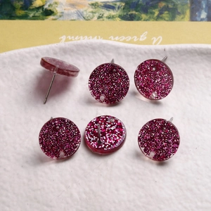 Pink glitter acrylic round stud earrings set with six pieces on a ceramic tray
