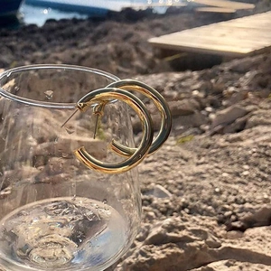 Klobige vergoldete C-förmige Hohl-Creolen an einem Glasrand unter natürlichem Sonnenlicht