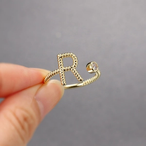 Detail eines verstellbaren Goldrings mit strukturiertem R-Buchstaben und rundem Zirkon
