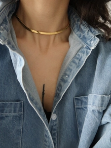 Golden flat snake bone necklace in polished stainless steel worn over a blue denim shirt