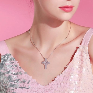 Iced out cross pendant necklace with sparkling zircons worn by model on pink background