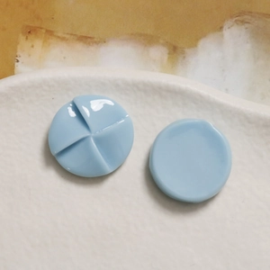 Macro detail of 20mm light blue resin windmill charms with glossy texture on ceramic tray