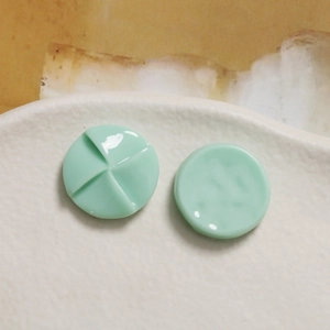 Macro view of mint green resin windmill charms on a textured white ceramic background