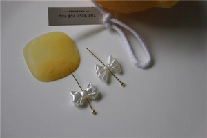 Detail of two pearl-white bow charms with gold pins for DIY nail art and shoes
