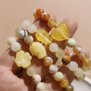 Close-up of stacked beaded bracelets with heart and clover charms in warm tones