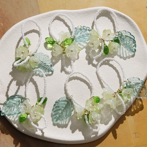 Détail de bagues perlées faites main avec fleurs de muguet et pendentifs feuilles