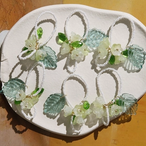 Vue détaillée de bagues artisanales en perles avec fleurs de muguet vertes sur un plat blanc