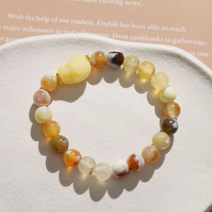 Detailed close-up of a resin beaded bracelet featuring a Pi Xiu charm on a white ceramic plate