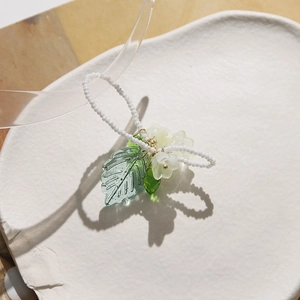 Détail d'une bague perlée à la main avec feuille transparente et breloques florales