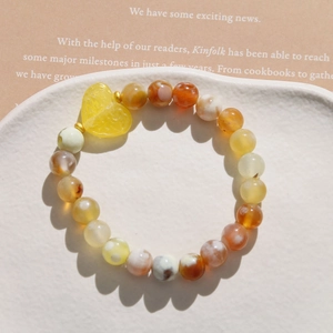 Detailed macro of a beaded bracelet featuring orange-yellow agate beads and a resin heart charm