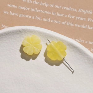 Macro shot of yellow resin flower beads and jewelry making pin on ceramic tray