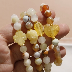 Handheld stack of beaded bracelets featuring agate and clover resin charms with gold spacers