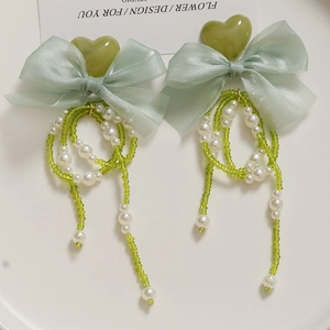 Detail of light green organza bow earrings with pearly tassels and heart resin charms