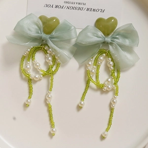 Detail of beaded bow earrings featuring heart charms and long pearl chain tassels