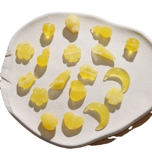 Translucent yellow resin beads in heart, moon, and flower shapes on a white ceramic plate