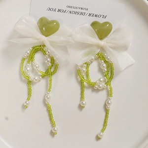 Detail of green heart resin charms with organza bows and pearl tassels for DIY crafts