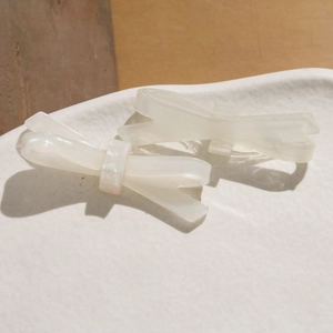Détail de deux grandes barrettes nœud en acétate blanc crème avec fini nacré sur un plateau