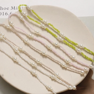 Detail of four handmade pearl chain charms with colorful beads on a ceramic tray