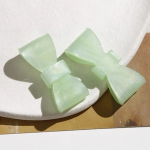 Detailed macro view of light green bow hair clips with pearlescent finish and gold glitter