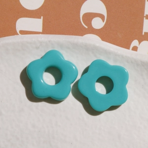 Close-up of teal resin flower charms with center hole on white ceramic plate