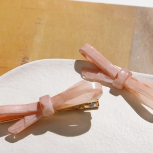 Détail de barrettes à cheveux nœud en acétate marbré rose avec base en métal doré sur plat