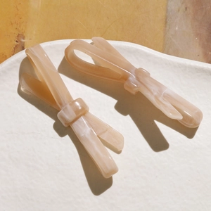 Détail de barrettes à nœuds en acétate effet marbré posées sur un plateau blanc élégant