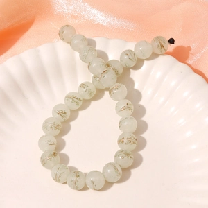 Macro detail of 13mm light green glass beads with gold patterns on a white shell plate
