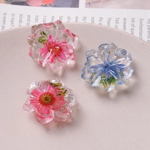 Detail of three handmade clear resin dried flower charms in pink, purple and red tones