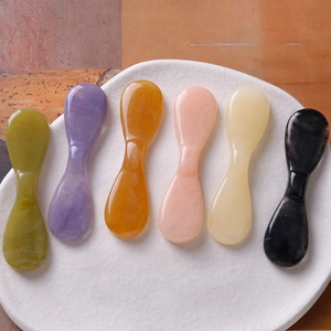 Détail de six outils de massage facial en résine avec texture marbrée sur une plaque
