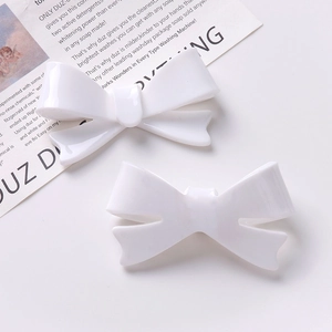 Detail view of two white acrylic bow hair clips on a minimalist newspaper background