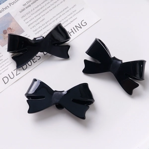 Three elegant black glossy bow hair clips displayed on a vintage magazine background