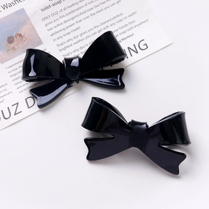 Detail of two black acrylic bow hair clips displayed on vintage background paper