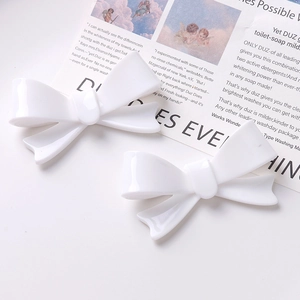 Detail of two white acrylic bow hair clips showing glossy finish on retro magazine