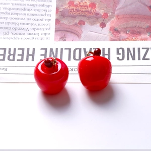 Dettaglio macro di ciondoli a mela in resina rossa con anelli dorati per gioielli fai da te
