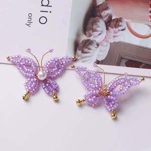 Macro detail of handmade purple beaded butterfly earrings with white pearls and gold accents