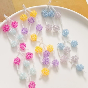 Macro detail of colorful beaded berry charms for DIY jewelry making in a white ceramic dish