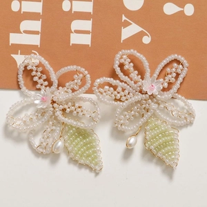 Detail of handmade beaded flower earrings with white petals, green leaf, and drop pearl