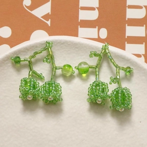 Macro detail of handmade green beaded cherry earrings on a white textured ceramic plate