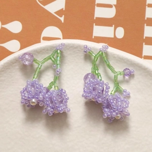 Macro shot of handmade purple beaded grape earrings with green stem on a white plate
