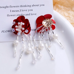 Détail de boucles d'oreilles fleurs rouges avec glands en perles sur assiette blanche