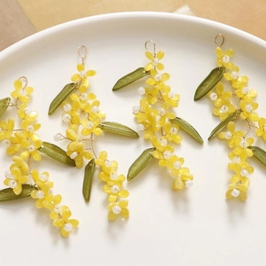 Handmade beaded flower charms with yellow petals and green leaves in a white ceramic dish