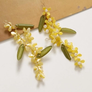 Detailed close-up of handmade floral tassel earrings with yellow blossoms and green leaves