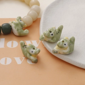 Detail of light green ceramic crocodile beads and a DIY dinosaur bracelet on a ceramic tray