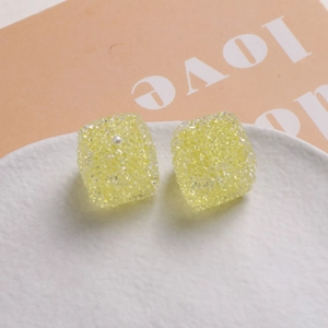 Vue détaillée de perles cubes en résine jaune texturée avec accent perle sur plateau
