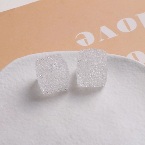Détail macro de clous d'oreilles carrés en résine pailletée de 16mm sur assiette blanche
