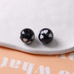 Vue macro de perles en résine noire de 16mm avec motifs de cœur blanc pour bijoux DIY